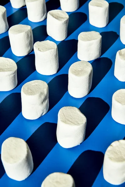 白いマシュマロの円筒形の列の多くは青色の背景にあります 不健康なジャンキー食品のパターン お菓子の柄 — ストック写真