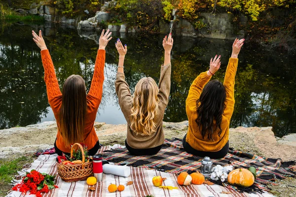 Three women best friends at autumn picnic in the park. Colorful plaid, thermos and pumpins. Friends having fun outdoors. Warm autumn October day