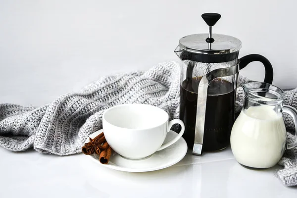French Press coffee and milk on the white table with sweater background. Morning coffee. Cinnamon sticks and anise star.