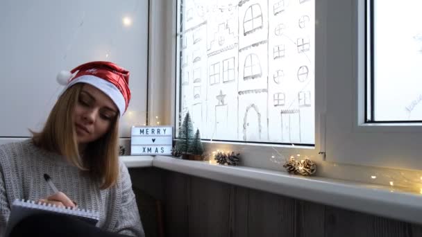 Una ragazzina che scrive una lettera a Babbo Natale. Decorato per Natale, si prepara per le vacanze. Spirito natalizio, vacanze e festeggiamenti concetto 4K. — Video Stock