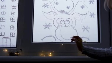 Kadın eli pencere camına Noel tatili geyiği çizer. Yeni yıl manzarası. Çelenk ışıkları. Hygge, dekorasyon ve noel konsepti. Evet. Kendin yap.
