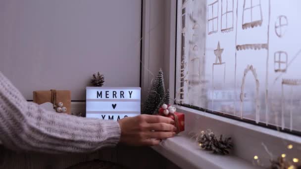 Chica joven sosteniendo la Navidad y la caja de regalo de año nuevo. Habitación con decoraciones navideñas. Luz de guirnalda. Regalos navideños. Feliz Navidad. — Vídeo de stock