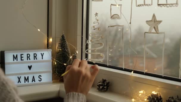 Żeńska ręka rysuje świąteczne dekoracje na szkle okiennym. Noworoczne krajobrazy. budynki miejskie girlandy światła. hygge, dekoracja i koncepcja Bożego Narodzenia — Wideo stockowe