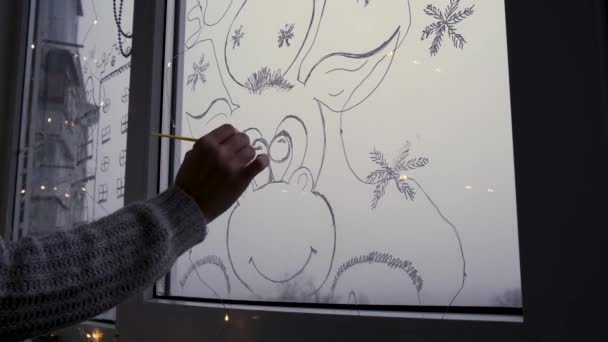 La mano femminile disegna il cervo di vacanze di Natale su vetro di finestra. Paesaggio di Capodanno. ghirlande luci. hygge, decorazione e concetto di Natale. Fai da te. Fallo da solo. — Video Stock