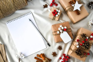 Şampanya renkli ipek arka planda hediyelerle dolu sıfır atık Noel metni. Defter boş Kopyalama alanı. Kartondan etiketli çevre dostu bir hediye. Yeni Yıl