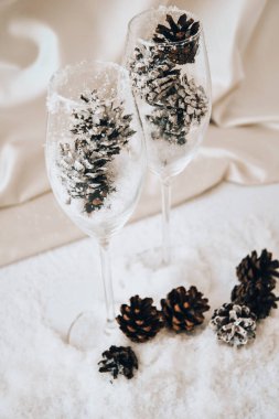 Beyaz karda süslü kozalaklı şampanya bardakları. Noel süsleri. Mutlu yıllar. Uzayı kopyala Mumlar. DIY ev yapımı dekor. sıfır israf noeli