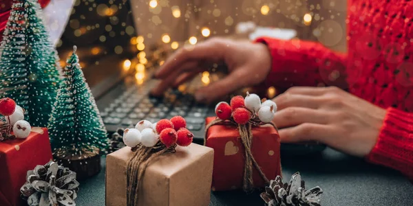 Christmas online shopping, work and education. New Year decorations on table. Woman with notebook computer at home. Winter holidays sales. Gift boxes, christmas trees. Garland light