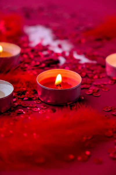 Burning red candles on Red shiny confetti sequinned background with feathers. Saint Valentines Day and Christmas background . Holidays background and textures.