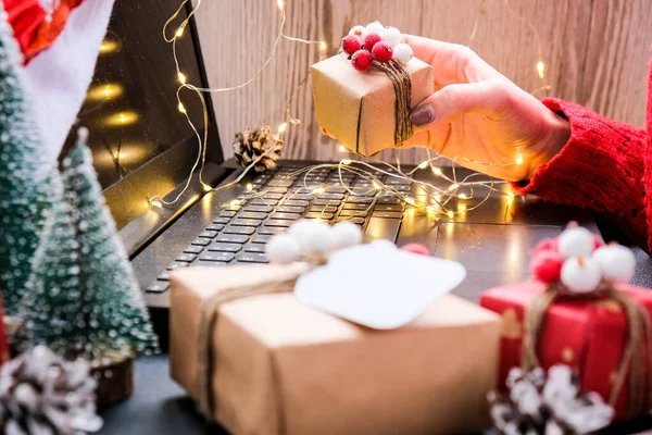 小さなプレゼントボックスを手に持ち ラップトップで検索を使用している女性 クリスマスのコンセプト オンラインショッピング 休日の販売 新年だ ガーランドライト — ストック写真