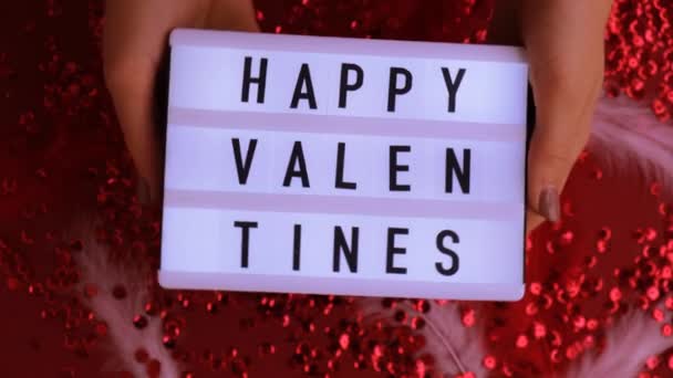 Vrouwelijke hand met lichtbak met tekst HAPPY VALENTINES op feestelijke rode achtergrond. St. Valentijnsdag, vakantie concept. — Stockvideo