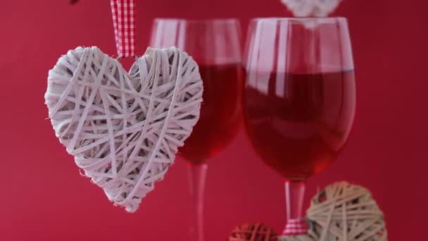 두 잔의 붉은 포도주와 흰 하트 장식이 빨간 배경 위에 드리워져 있습니다. 발렌틴 데이 컨셉 축하 해. 사랑과 로맨스. 낭만적 인 데이트. — 비디오