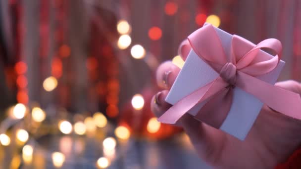 Hadiah Natal di tangan seorang wanita di Karangan bunga bokeh ringan. Fokus selektif. Valentines hadir. Salin ruang. — Stok Video