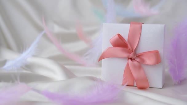 Plumes d'oiseau volant dans une boîte-cadeau blanche avec ruban rose. Concept de vacances moelleux et délicat. — Video
