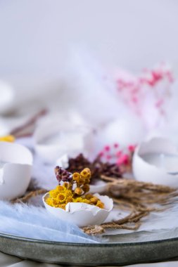 Paskalya bayramı. Kendiniz yapın. Moda Paskalya dekorasyonları. Kuru otlu organik yumurtalar ve tabakta kuru çiçekler. Yumurtaların beyaz kabuğunda mum. Kuş tüyü. Uzayı kopyala Tebrik kartı. Pastel renkler.