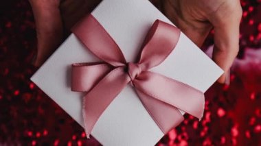 Kırmızı arka planda pembe kurdeleyle süslenmiş bir kutuyla kadın eli uzanıyor. Sevgililer günün kutlu olsun. Anneler Günü videosu. Yakınlaştır