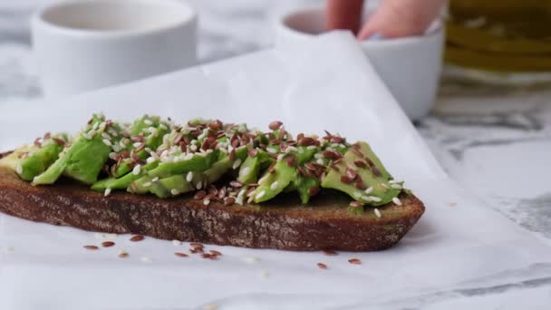 Kvinnlig hand gör Friska avokado toast på träskiva. Sesamfrön och linfrön. Vegetarisk mat. — Stockvideo