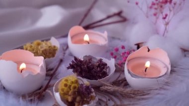 Moda Paskalya dekorasyonları. Tabağında kuru çim çiçekleri olan organik yumurtalar. Yumurtaların beyaz kabuğunda mum ışığı. Kuş tüyü. Yanan mumlar alev dumanı