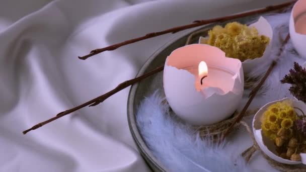 Trendy paasversieringen. Gebarsten biologische eieren met droge gras bloemen op bord. Kaarslicht in de witte schaal van de eieren. Vogelveer. Brand kaarsen vlam rook — Stockvideo