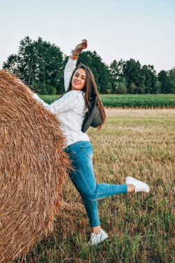 Kovboy şapkalı kadın saman balyasının yanında kalıyor. Yaz, güzellik, moda, cazibe, yaşam tarzı konsepti. Cottagecore çiftliği doğaldır.