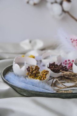 Paskalya bayramı. Kendiniz yapın. Moda Paskalya dekorasyonları. Kuru otlu organik yumurtalar ve tabakta kuru çiçekler. Yumurtaların beyaz kabuğunda mum. Kuş tüyü. Uzayı kopyala Tebrik kartı. Pastel renkler.