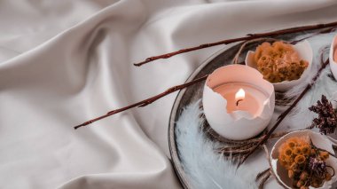 Paskalya bayramı. Kendiniz yapın. Moda Paskalya dekorasyonları. Tabağında kuru çim çiçekleri olan organik yumurtalar. Yumurtaların beyaz kabuğunda mum ışığı. Kuş tüyü. Uzayı kopyala Paskalya kartı. Pastel renkler.