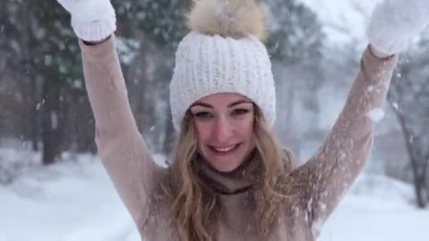 Kerstmis, vakantie en winterseizoen concept. Jonge gelukkige vrouw blaast spelen met sneeuw in de winter bos natuur. Slow motion Warme kleding gebreide handschoenen en muts. — Stockvideo