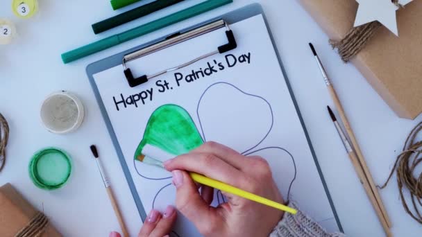 Female hands painting greeting card St Patricks day. Gift idea, decor craft. DIY. Do it yourself. Clovers, brush and paint. — Stock Video