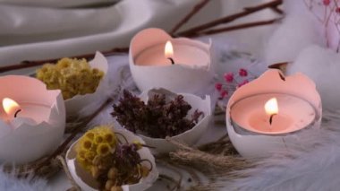 Moda Paskalya dekorasyonları. Tabağında kuru çim çiçekleri olan organik yumurtalar. Yumurtaların beyaz kabuğunda mum ışığı. Kuş tüyü. Yanan mumlar alev dumanı