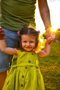 Şirin küçük kız babasıyla el ele tutuşuyor. Çocuk imajıyla yürümek. Küçük kız ailesiyle el ele tutuşuyor. Gülümseyen bebek elbisesi içinde.