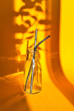 Cam şişede yeniden kullanılabilir metal pipetler, sarı arka planda su, paslanmaz çelik, çevre dostu pipet seti. Sıfır kayıp. Plastiksiz. Paslanmaz Çelik Çubuklar. Yaratıcı kavram