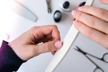 Kadın eli, tırnak cilası, manikür aletleri, masa üstü düzlüğü. Ev konseptinde manikür yapmayı. Evde kalarak manikür yapsana. Kişisel bakım. Çıplak tırnaklar. Spa, ilaç reklamı. Güzellik.