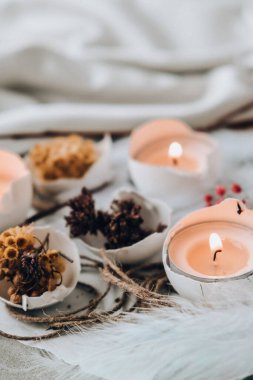 Paskalya bayramı. Kendiniz yapın. Moda Paskalya dekorasyonları. Tabağında kuru çim çiçekleri olan organik yumurtalar. Yumurtaların beyaz kabuğunda mum ışığı. Kuş tüyü. Uzayı kopyala Paskalya kartı. Pastel renkler.