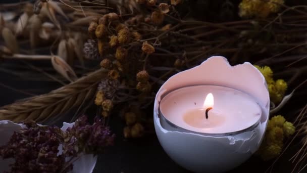 Burning candle Trendy Easter decorations. Cracked organic eggs shell with dry grass and dry flowers candle light. Dark background. — Stock Video