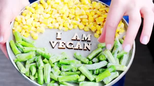 Női kéz fogja VEGAN VAGYOK szöveget a tányéron. Veganizmus, vegetáriánus egészséges életmód. Egészséges vegetáriánus, zöldbab sárga kukorica — Stock videók