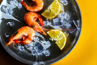 Gri tabakta limonlu ve buzlu kırmızı karides ve sarı arka plan. Moda renkleri. İzometrik biçimdeki minimalist kavram