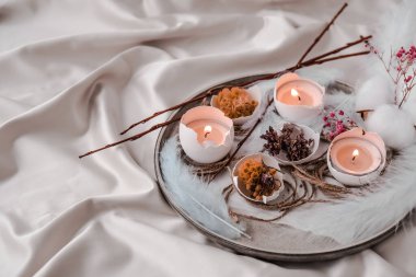 Paskalya bayramı. Kendiniz yapın. Moda Paskalya dekorasyonları. Tabağında kuru çim çiçekleri olan organik yumurtalar. Yumurtaların beyaz kabuğunda mum ışığı. Kuş tüyü. Uzayı kopyala Paskalya kartı. Pastel renkler.