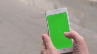 Yeşil ekranlı cep telefonu kullanan 4K kadın eli. Krom anahtar. Sokakta mobil uygulama