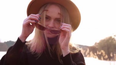 Yavaş hareket eden beyaz, siyah kazaklı, bej şapkalı sarışın kadın kırsalda güneş gözlüğü takıyor. Altın saat, Cottagecore. Yerel seyahat. Yavaş yaşam. Ruh Sağlığı