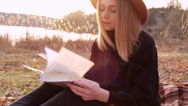 Lassú mozgású, fehér, szőke nő bézs kalapban fekete pulóverben könyvet olvas vidéken. Arany óra, házikó. Helyi utazás. Lassú élet. Mentális egészség — Stock videók