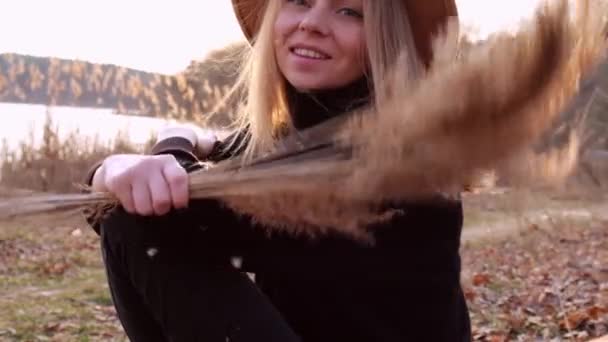 Caucasian blonde woman waving pampas grass with beige hat in black sweater in the countryside. Golden hour, cottagecore. Local travel. Slow living. Mental health — Stock Video