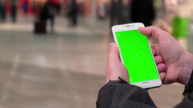 Yeşil ekranlı cep telefonu kullanan 4K kadın eli. Krom anahtar. Alışveriş Merkezi 'nde mobil uygulama. Arka planda yürüyen insanlar