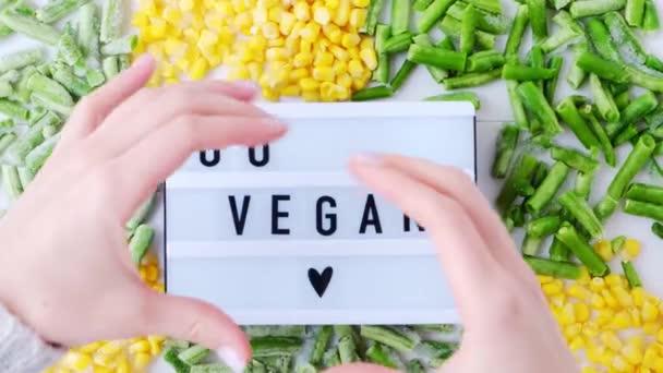 Руки женщины держат Lightbox с текстом GO VEGAN замороженные овощи продукты из желтой кукурузы, зеленые бобы. Сохранение продовольствия на зиму. — стоковое видео