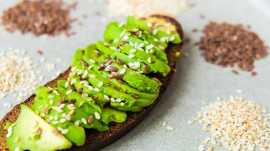 Beton zeminde sağlıklı avokado tostu. Kepekli ekmek, susamlı keten tohumu. Vejetaryen keto diyeti. Sağlıklı beslenme. Vejetaryen Moda Guacamole Sandviçi.