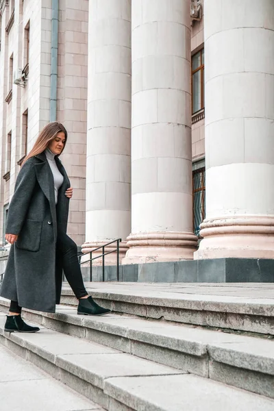Young brunette woman walking up on stairs. Long beautiful hair and long coat in business downtown. Careerist. Women career. Businesswoman. — Stock Photo, Image