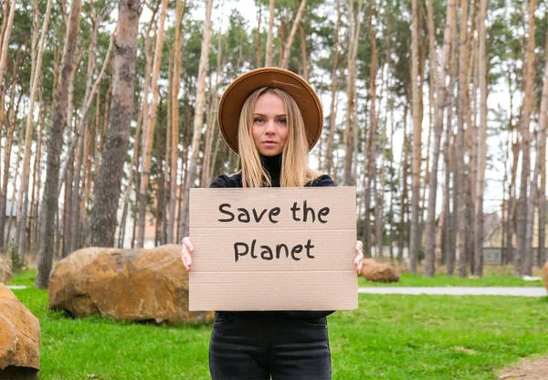 Portret van een blanke jonge vrouw met een hoed die karton vasthoudt met tekst buiten. Natuur achtergrond. Demonstrant activist — Stockfoto