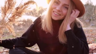 Beyaz, sarışın bir kadın kırsalda bej şapkalı, siyah kazaklı otlar sallıyor. Altın saat, Cottagecore. Yerel seyahat. Yavaş yaşam. Ruh Sağlığı