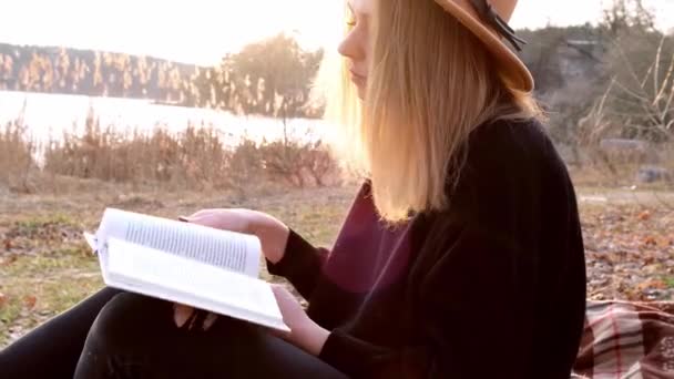 4k donna bionda caucasica con cappello beige in maglione nero legge libro in campagna. Ora d'oro, Cotttagecore. Viaggi locali. Una vita lenta. Salute mentale — Video Stock