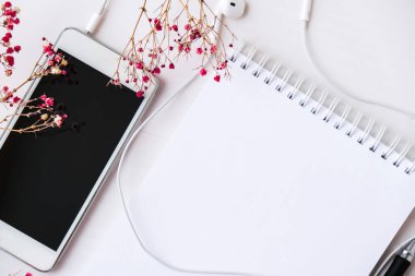 Kulaklıklı cep telefonlu boş bir defter aç. Siyah ekran ve siyah kalem. Kuru pembe çiçek süslemesi. İş yeri. Düşman metni kopyala. Üst Manzara. Pastel renkler