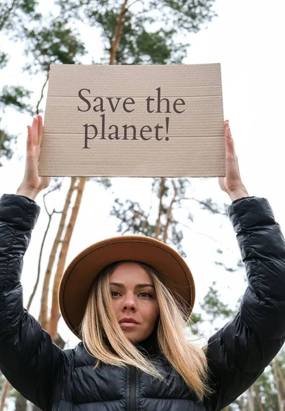 Porträt einer kaukasischen jungen Frau mit Hut, die im Freien einen Karton mit Text hält. Natur im Hintergrund. Protestaktivist — Stockfoto