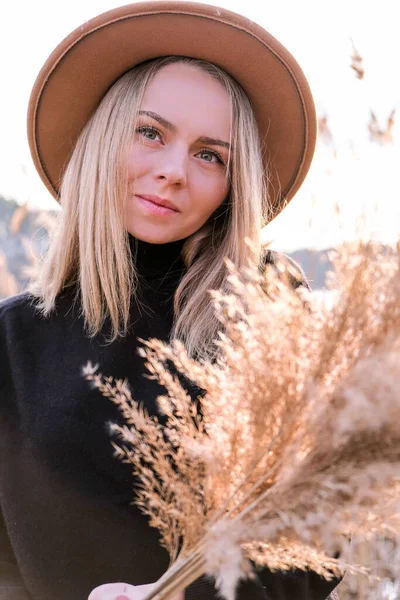 Mujer rubia europea con sombrero beige en suéter negro en el campo. Hora dorada, casa de campo. Viajes locales. Una vida lenta. Salud mental. Hierba pampeana —  Fotos de Stock